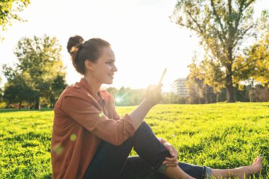 Parkta dışarıda dinlenirken akıllı telefon kullanan bir kadın çevrimiçi mesaj atıyor.