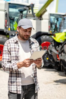 Tarım makineleri bayisinde dijital tablet kullanan erkek işçinin dikey fotoğrafı.