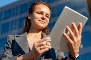 Modern Kafkasyalı iş kadını şehir sokaklarında dijital tablet kullanıyor ve gülümsüyor.