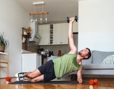 Kafkasyalı adam evde yoga minderinde halterle egzersiz yapıyor..