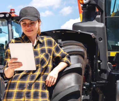 Kadın, tarım veya inşaat makinelerinin yanında duruyor ve dijital tablet üzerindeki kira sözleşmesini okuyor
