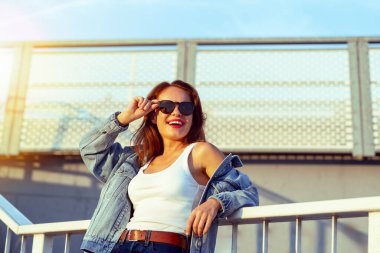 Neşeli şehir kadını güneş gözlüğü takıyor. Şehir caddesindeki merdivenlerde dikiliyor.
