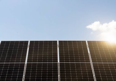 Mavi gökyüzünün arka planında güneş ışığı olan siyah güneş panelleri
