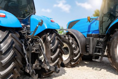 Mavi traktörlerin arka görüntüsü bir çiftlik arazisi bayisinde sergileniyor.