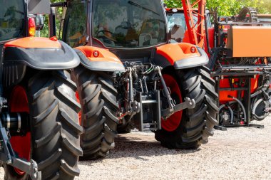 Turuncu traktörlerin arka görüntüsü bir çiftlik arazisi bayisinde sergileniyor.