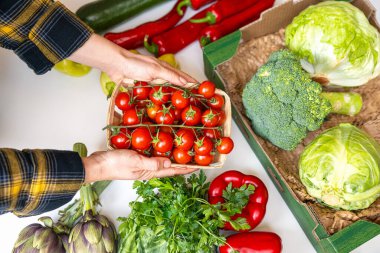 Bakkaldan aldıklarınızı paketlere yerleştirin. Kadın eli, masanın üzerinde sebzeli kiraz domatesli kutuyu tutuyor..