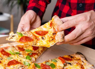 Erkek ellerinde bir dilim pizzanın yakın çekimi.