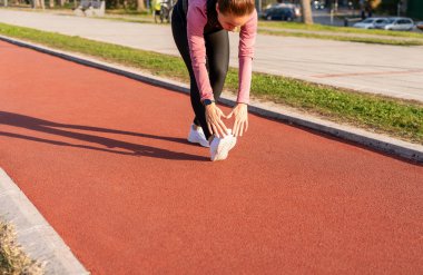 Kadın koşucu şehir caddesinde koşu pistinde ısınıyor.