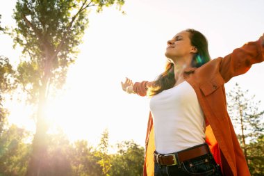 Doğayı kucaklayan, kollarını açmış barışçıl bir ortamda gülümseyen bir kadının düşük açılı görüntüsü..