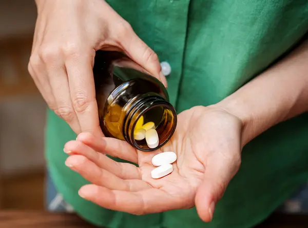 Kadın eline şişeden haplar dolduruyor.