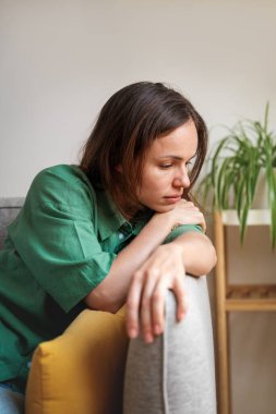 Üzgün ve yorgun bir kadın evdeki kanepede oturuyor ve aşağıya bakıyor.