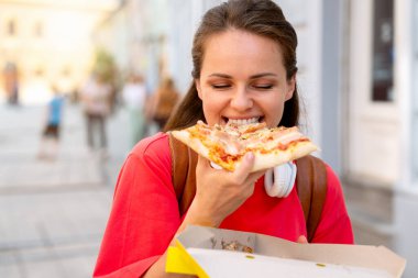 Şehirde sokakta yürürken pizza yiyen bir kadın..
