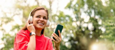 Kablosuz kulaklık ve akıllı telefonla müzikten hoşlanan gülümseyen kadın.