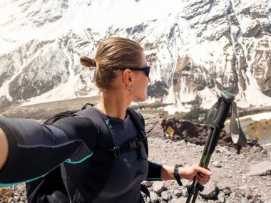 Yürüyüş direkleri ve sırt çantalı profesyonel bayan yürüyüşçü karlı dağlara karşı selfie çekiyor..