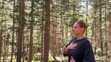 Dikkatli genç kadın orman doğasında nefes egzersizi yapıyor.