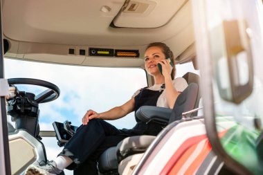 Kendine güvenen bir çiftlik işçisi traktörde otururken telefonla konuşuyor.