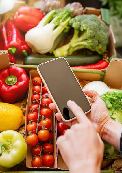 Cep telefonu taze organik sebze kutularının üstünde.