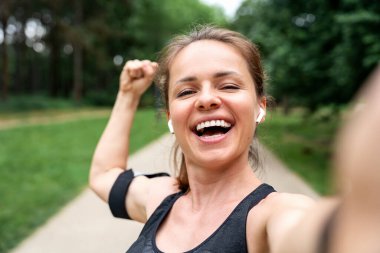 Neşeli kadın kaslarını esnetiyor ve açık hava antrenmanından sonra selfie çekiyor.