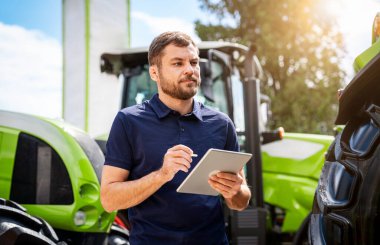 Tarım makineleri galerisinde dijital tablet kullanan çiftçi.