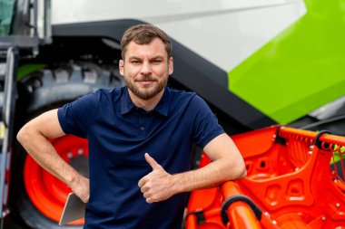 Erkek tarım sektörü profesyoneli, tarım bayiliğinde tarım makinelerinin yanında duruyor.