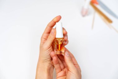 Beyaz arka planda küçük bir şişe tırnak içi yağı tutan kadın eller.