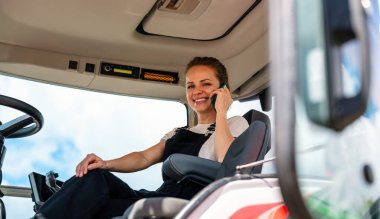 Kadın tarım makineleri sürücüsü kulübede cep telefonuyla konuşuyor.