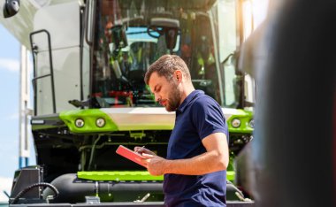 Tarım makineleri bayiliğinde hasatçının yanında tablet kullanan bir adam.