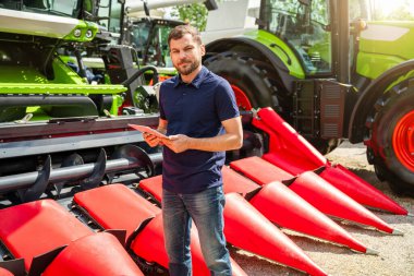 Dijital tabletli erkek satış temsilcisi tarım makineleri bayiliğinde hasat makinesinin yanında duruyor.. 