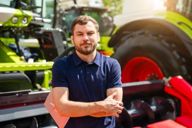 Teçhizat bayiliğinde tarım makinelerinin yanında dijital tabletli erkek tarım uzmanının portresi