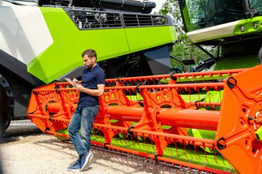 Tarım endüstrisi işçisi, malzeme bayiliğinde hasatçıyı birleştirerek tablet kullanıyor.