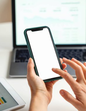 Dizüstü bilgisayarın arka planında akıllı telefon kullanan kadın elleri.