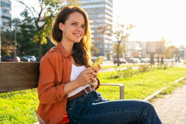 Şehir sokağında bankta oturan akıllı sesli genç bir kadın.