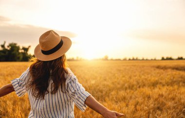 Gün batımında kırsal kesimdeki buğday tarlasında kendini özgür hisseden bir kadın.