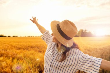 Hasır şapkalı kadın gün batımında mısır gevreği tarlasında doğanın tadını çıkarıyor.