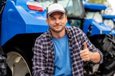 Modern çiftçi portresi gülümseyen ve arka planda makinelerle baş parmak gösteren