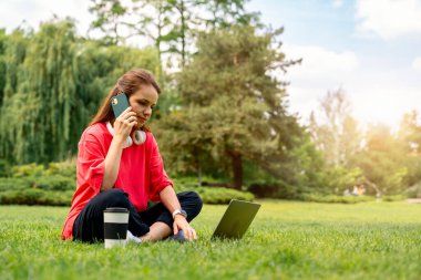 Genç bayan serbest çalışan dizüstü bilgisayar kullanıyor ve dışarıda telefonla konuşuyor.