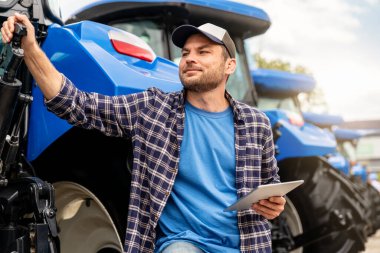Gururlu erkek çiftçi, traktörün yanında bir tablet tutuyor.