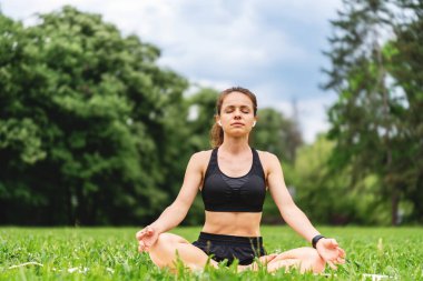 Modern kadının sağlıklı ve aktif yaşam tarzı. Lotuslu bir kadın yazın şehir parkında meditasyon yapıyor..
