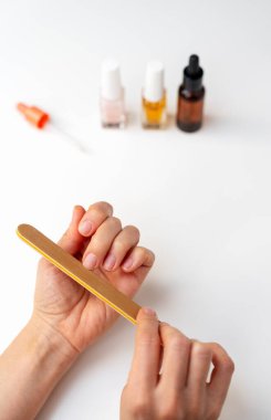 Beyaz masadaki tırnak törpüsüyle tırnaklarını törpüleyen kadın ellerine yakın plan.