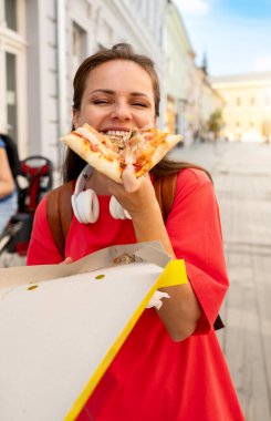 Şehir caddesinde pizza yiyen mutlu kız öğrenci.