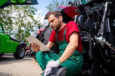 Teknisyen tarlada traktörü tabletle inceliyor.