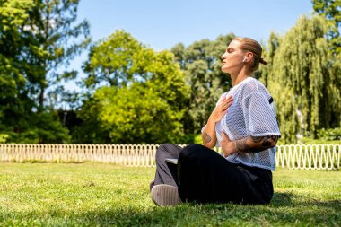 Şık bir genç kadın şehir parkında farkındalık ve nefes egzersizi yapıyor.