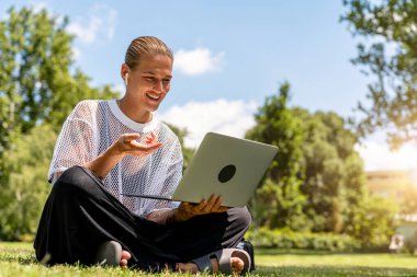 Genç, şık bir kadın parkta dizüstü bilgisayarla uğraşırken sanal bir görüşme yapıyor.