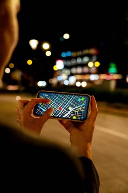 Gece şehir caddesinde navigasyon için akıllı telefon kullanan bir kadın.