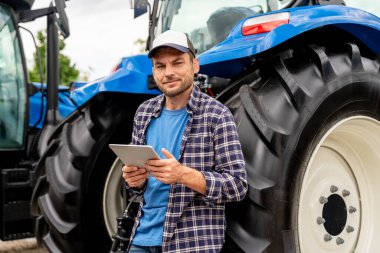 Açık havada traktörle tablet tutan bir tarım işçisi.