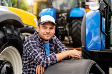 Tarımsal ekipman parkında traktörlerin yanında duran kırsal adam.