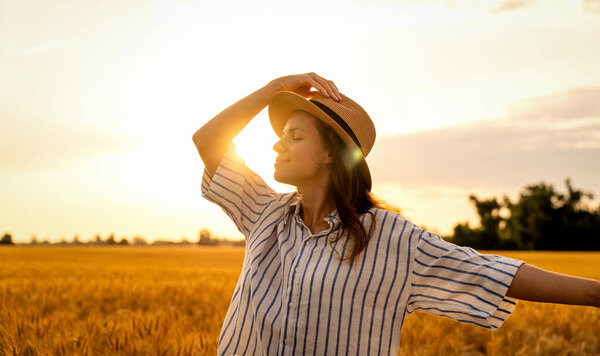 Serene woman in straw hat enjoying peaceful countryside at sunset