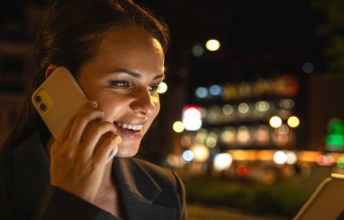 Modern kadın girişimci cep telefonuyla konuşuyor ve şehir caddesinde tablet kullanıyor.