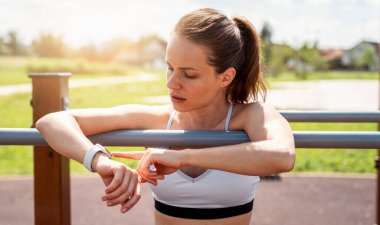 Açık spor salonunda spor yapmak için akıllı kaset kullanan zinde genç bir kadın.