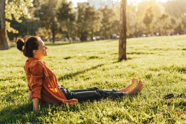 Şehir parkında çıplak ayakla dinlenen genç bir kadın.